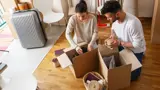 A couple packing boxes on the floor of their home in preparation for moving house.